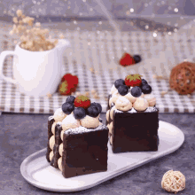 two pieces of chocolate cake with strawberries and blueberries on top on a white plate