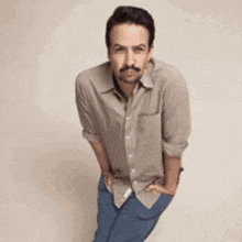 a man with a mustache is standing with his hands in his pockets and looking at the camera .
