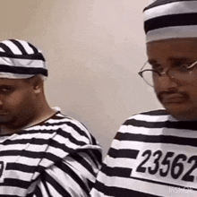 two men dressed as prisoners are standing next to each other wearing striped uniforms and hats .