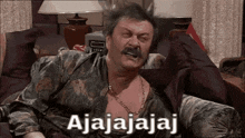 a man with a mustache is sitting on a couch with ajajajaj written on the screen