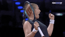 a woman holding a tennis racquet in front of a sign that says now sports live