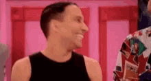 a man in a black tank top is smiling while standing in front of a pink wall .