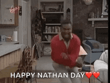 a man in a red sweater is dancing in a living room with the words `` happy nathan day '' .