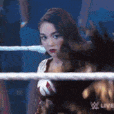 a woman is standing in a wrestling ring with a w live logo on the bottom right corner .