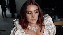 a woman with red hair and a pearl necklace looks down