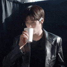 a man wearing a leather jacket drinks from a white cup