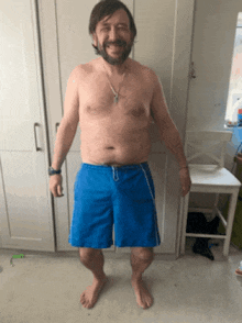 a shirtless man wearing blue shorts is standing in front of a chair