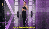 a woman is standing on a stage with purple lights and says i 'm at heart a lazy bitch .