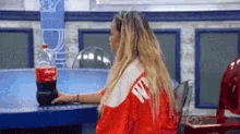 a woman in a red and white jacket is holding a bottle of coke .