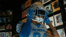 a football player wearing a memphis jersey and helmet stands in front of a wall of cds