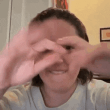 a woman is making a heart shape with her hands over her eyes .