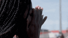 a woman with braids is praying with her hands folded in front of her face