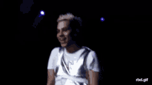 a man wearing a white shirt and a silver vest is standing on a stage in the dark .