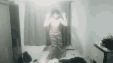 a boy without a shirt is jumping on a bed in a room