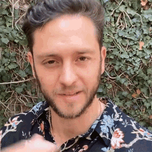 a man with a beard wearing a floral shirt looks at the camera