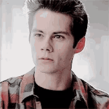 a young man wearing a plaid shirt and a black shirt looks at the camera .