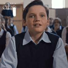 a young boy sitting in a classroom with the words son of a gitch on the bottom right