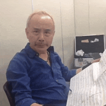 a man in a blue shirt is sitting in a chair reading a piece of music .