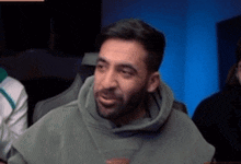 a man with a beard wearing a green hoodie looks at the camera