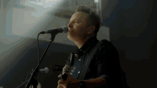 a man singing into a microphone with a guitar in front of him