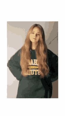 a woman with long blonde hair is wearing a green sweatshirt that says uah on the front