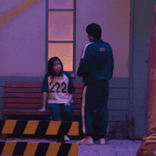 a girl wearing a 222 shirt sits on a bench next to a man