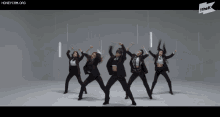 a group of women in tuxedos are dancing in front of a white wall