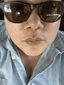 a close up of a woman wearing sunglasses and a denim shirt
