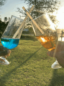two glasses with straws in them are being held in someone 's hand