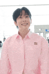 a young man wearing a pink shirt with the word miu on the sleeve is smiling .