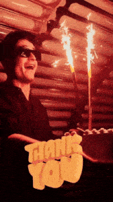 a man wearing sunglasses is holding a cake with candles and a thank you sign