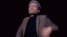 a man in a suit and black turtleneck is dancing on a stage .