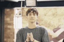 a young man in a gray shirt is clapping his hands in a room .