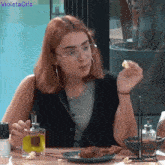 a woman sitting at a table with a plate of food and a glass of olive oil