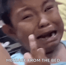 a young boy is crying and giving the middle finger with the words message from the bed below him .