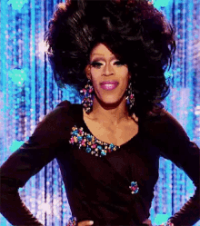 a drag queen is wearing a black dress and earrings and has a large afro .