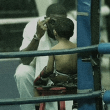 a man sits on a stool in a boxing ring talking to a little boy