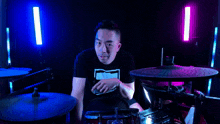 a man playing drums in a dark room with a blue and pink light behind him