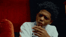 a young man in a white shirt with the letter g on it is sitting in front of a red curtain .