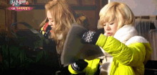 a woman in a yellow jacket is holding a black object in her hand