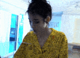 a woman wearing a yellow shirt with a pattern on it looks down at something