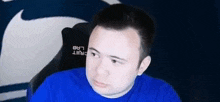a man in a blue shirt is sitting in a chair and making a face .