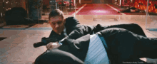 a man in a suit is holding a gun while another man lays on the floor
