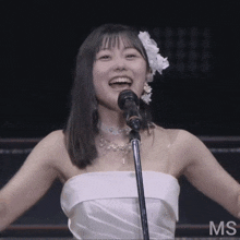 a woman in a white dress singing into a microphone with the letters ms on the bottom right