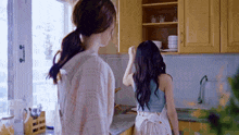 two women standing in a kitchen looking at a stack of bowls on a shelf