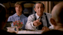 a man and a woman are sitting at a table and the man is pointing at something