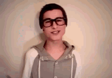 a young man wearing glasses and a beanie is smiling while wearing a hoodie .