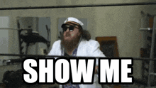 a bearded man in a white suit stands in a boxing ring with the words show me above him