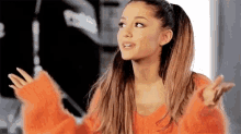 ariana grande is wearing a red sweater and making a funny face .
