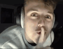 a young man wearing headphones is making a shhh gesture .